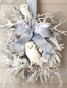 two white owls sitting on top of a wreath with pine cones and silver ribbon around it