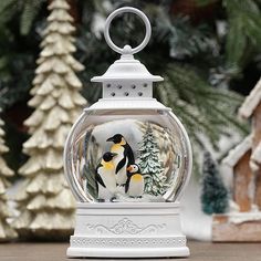 a snow globe with two penguins in it on a wooden table next to christmas trees