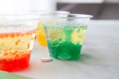 two cups filled with colored liquid sitting on top of a table next to each other