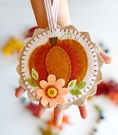 a hand holding an ornament with two oranges on it and a flower