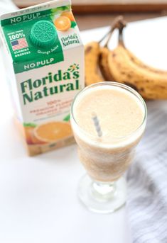 a drink in a glass next to a banana and carton of nut milk on a table