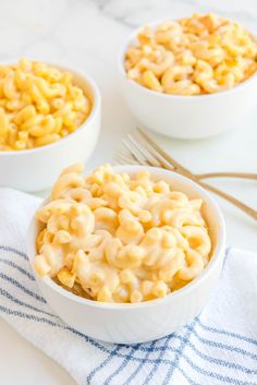 two bowls filled with macaroni and cheese on top of a white tablecloth