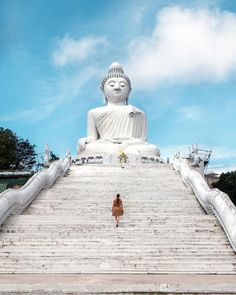 a woman standing in front of a giant buddha statue with stairs leading up to it