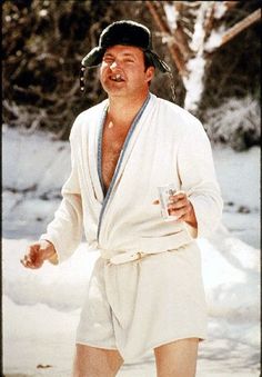 a man in white robe and hat standing on snow covered ground holding a can of soda