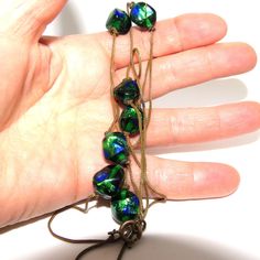 An art nouveau necklace with a spring-ring clasp made from finally woven brass chain. The chain is set with seven large chunky green and blue glass peacock eye beads, held in place by tightly knotting the chain before and after each bead. The necklace measures about 77 cm long, and each bead is about 1.3 cm long by 1.2 cm wide, irregularly shaped. The necklace is in great condition, and would be a wonderful accent piece to go with a shorter art nouveau necklace, especially one set with peacock eye glass! Green Glass Jewelry With Adjustable Chain, Art Nouveau Necklaces, Lansing Mi, Eye Glass, Eye Beads, Brass Chain, One Set, Green And Blue, Spring Rings