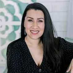 a woman with long black hair smiling at the camera and wearing a polka dot shirt