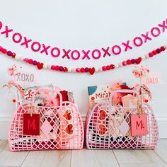 two pink baskets filled with valentine's day items on top of a wooden floor