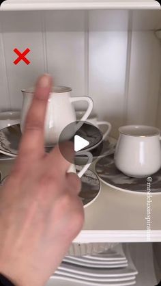 a person is pointing at the dishes on the shelf