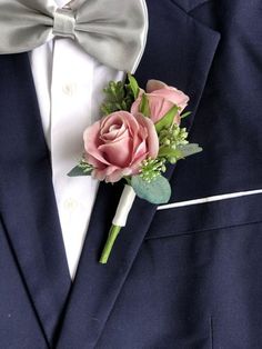 a boutonniere with pink roses and greenery on the lapel of a suit