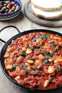 a pan filled with food sitting on top of a table next to bread and olives