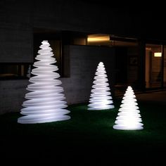 three white christmas trees are lit up in the dark at night, with grass on the ground