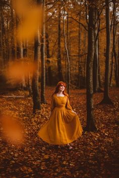 a woman in a yellow dress is walking through the woods with leaves on the ground