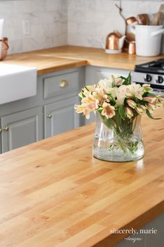 a vase filled with flowers sitting on top of a wooden countertop in a kitchen