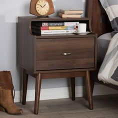 a nightstand with a clock and books on it next to a pair of brown boots