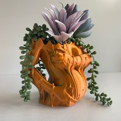 an orange vase with flowers in it sitting on a white table top next to some green leaves