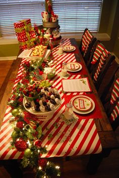 a christmas table setting with red and white striped table cloth, green garland, pine cones, candy canes