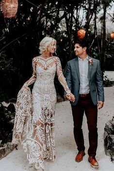 a man and woman holding hands walking down a path in front of some trees with lights