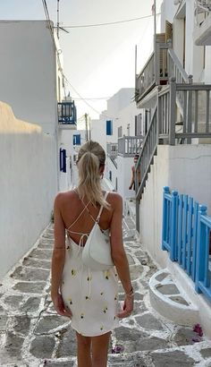 a woman in a white dress is walking down the street with her back to the camera