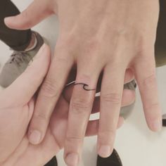 two people with wedding rings on their fingers holding each other's hand and the ring has a wave tattoo on it