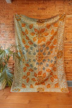 an orange and blue blanket sitting on top of a wooden floor next to a potted plant