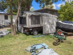 a trailer is parked in the grass next to a tree and some camping gear on the ground