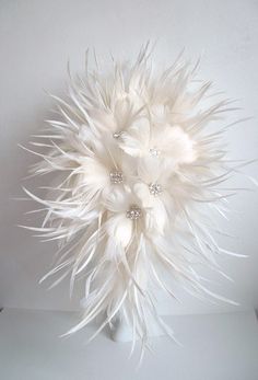 a white vase filled with lots of feathers and flowers on top of a table next to a wall