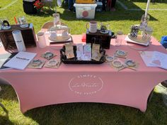 a pink table topped with lots of items on top of a lush green field covered in grass