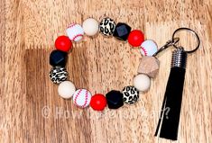 a baseball bracelet with red, white and black beads is on a table next to a tassel