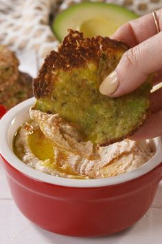 a person dipping some kind of food into a red bowl with an avocado in it