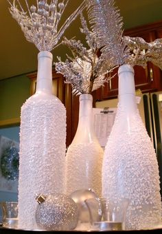 three white vases with silver flowers in them sitting on a counter top next to each other