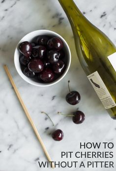 a bowl of cherries next to a bottle of wine and chopsticks on a marble table