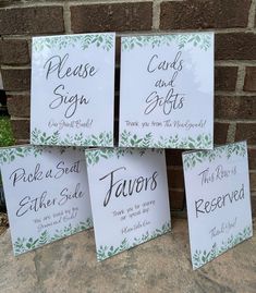 four white cards with green leaves on them are sitting next to a brick wall that says, please sign and gifts