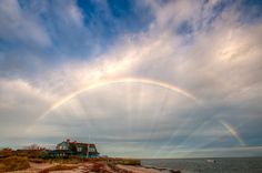 a house on the beach with a rainbow in the sky