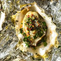 an open oyster shell covered in herbs and seasoning on tin foil with other food items