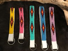 four key chains with beaded designs on them sitting next to a tree branch in the woods