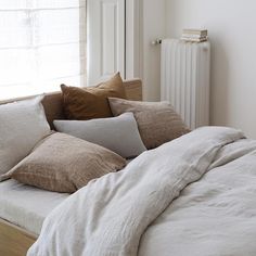 a bed covered in lots of pillows next to a window with a radiator