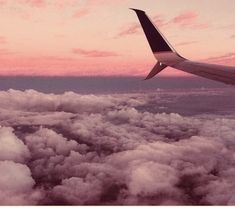 an airplane wing flying above the clouds at sunset or dawn with pink and purple hues