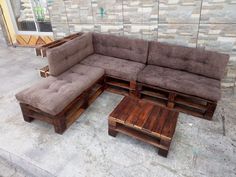 a couch made out of wooden pallets sitting on top of a cement floor next to a brick wall