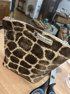 a giraffe print purse sitting on top of a wooden table next to scissors