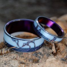 two wedding rings with blue and white marble inlays on top of a rock