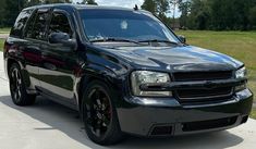 a black suv parked on the side of a road in front of a grassy field