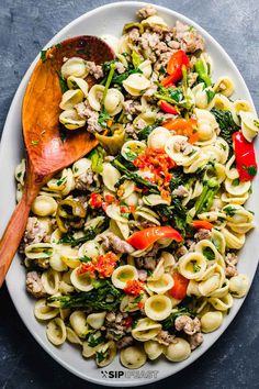 pasta salad with sausage, spinach and peppers on a white plate next to a wooden spoon