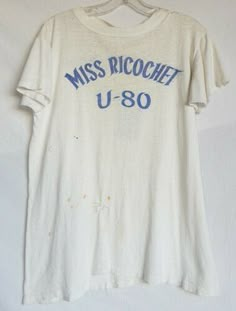 VINTAGE PRODUCTIONS Present 1960's Miss Ricochet U-80 Racing Team T-shirt. Short sleeve, thin cotton body. White body with blue printed designs n the front and back. Has some staining and two holes in the lower front that look like they had been hand repaired before. No tags. Has been well worn and used. Shoulder to shoulder: 17 1/2 inches armpit to armpit: 18inches sleeve length: 5 inches Bottom of collar to hem: 26 inches We only ship via Priority mail in in the US and out side the US it is do Vintage White T Shirt, Bar Merch, Haircut Shag, Pixie Cut Styles, Vintage Tee Shirts, Vintage Tennis, Wardrobe Pieces, Americana Fashion, Country Shirts