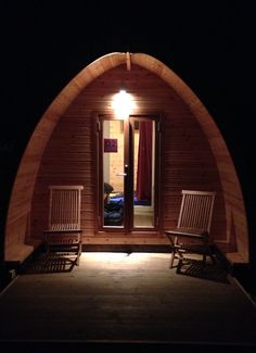 two wooden chairs sitting in front of a doorway at night with lights on the door