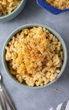 three bowls filled with macaroni and cheese on top of a gray surface next to silverware