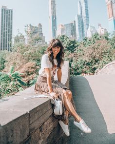 a woman is sitting on a wall with her hand in her pocket and smiling at the camera