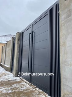 the side of a building with a large metal gate on it and snow covered ground