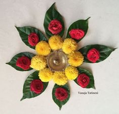 a flower arrangement with yellow and red flowers on a white table top next to green leaves