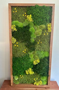 a wooden frame filled with green moss and yellow flowers on top of a wood table