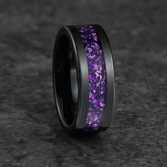 a purple and black wedding band with flowers inlaying the center, on a dark surface